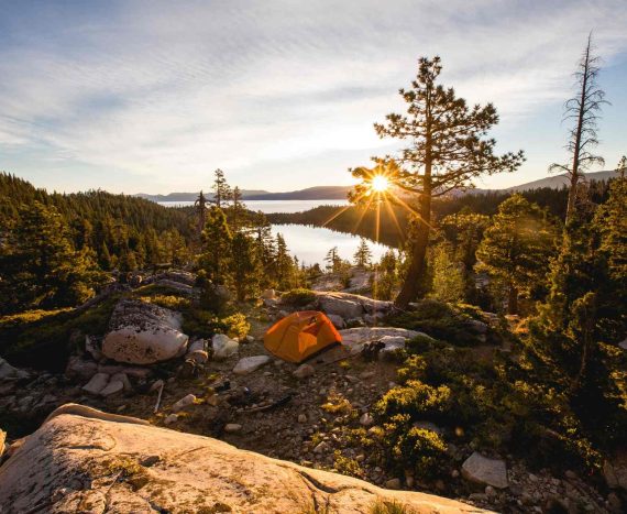 beautiful-shot-orange-tent-rocky-mountain-surrounded-by-trees-during-sunset.jpg